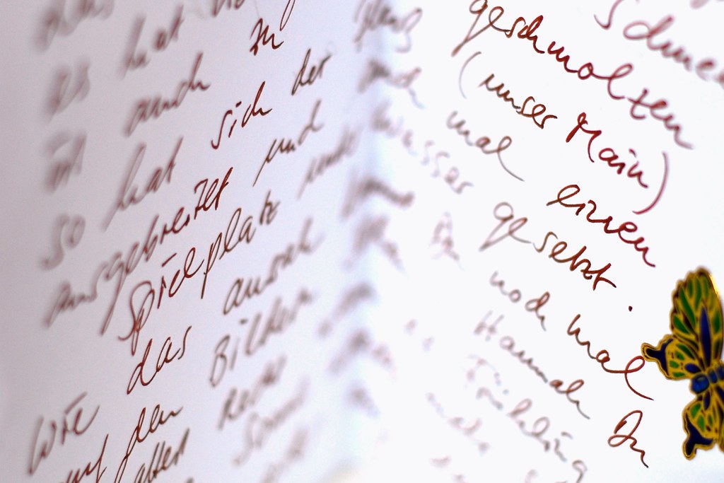 A hand writing a letter with a pen on a wooden desk